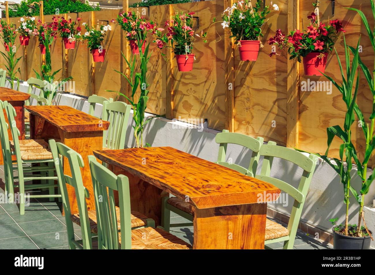 Empty restaurant outdoor seating area with wooden chairs and tables, decorated with flowers on red pots around. Stock Photo