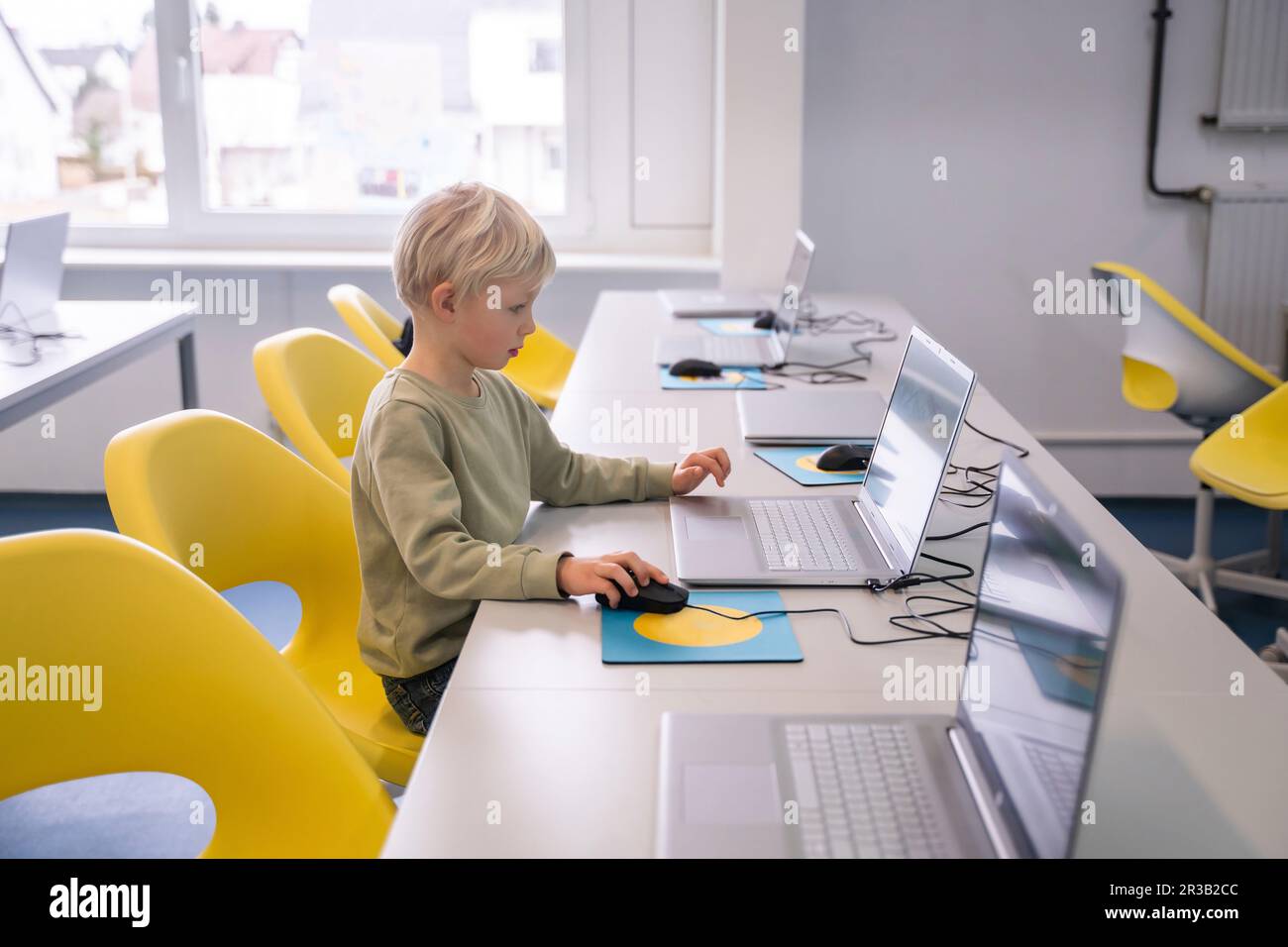 Blond boy using laptop sitting on chair at school Stock Photo - Alamy