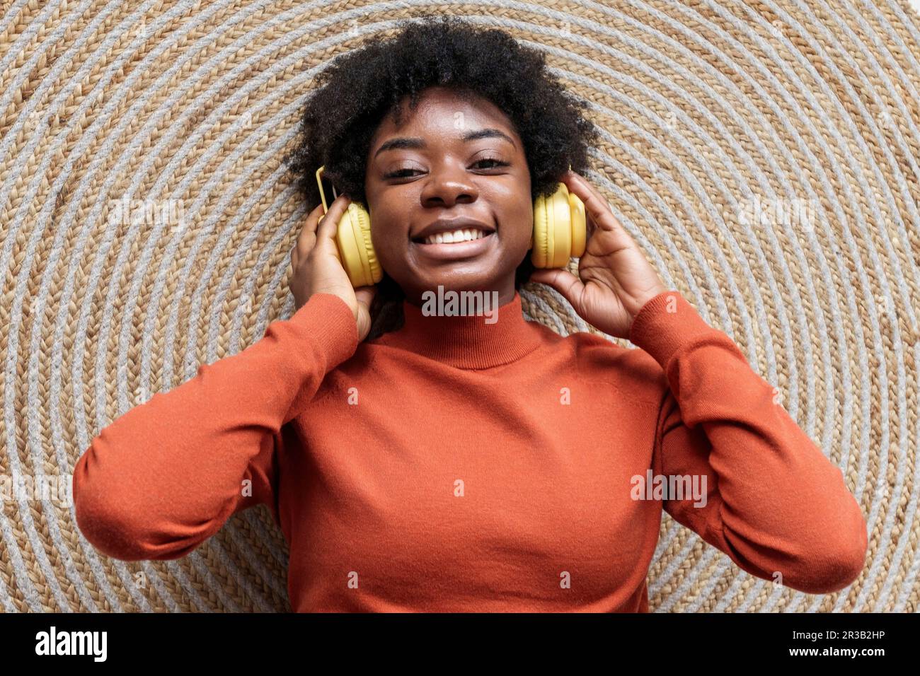 Smiling young woman lying on rug and listening to music through ...