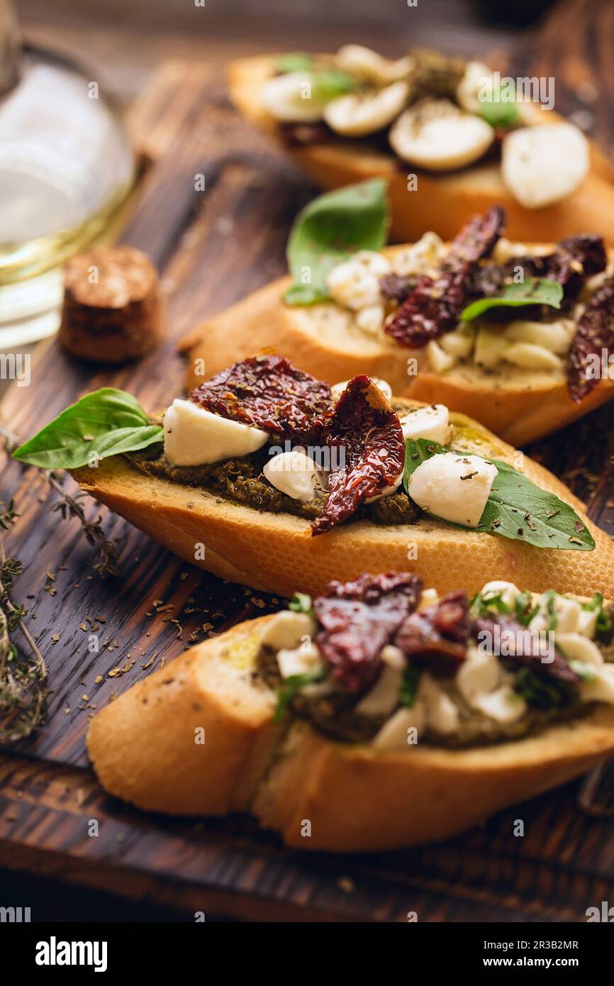 Sandwich with mozzarella cheese, pesto, sun-dried tomatoes and basil and thyme, served on the wooden Stock Photo