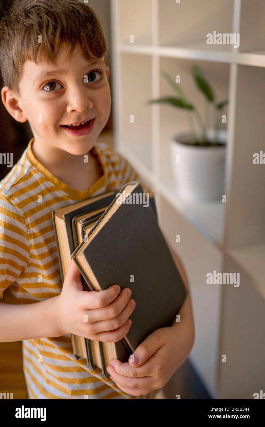 Smiling boy holding books at home Stock Photo