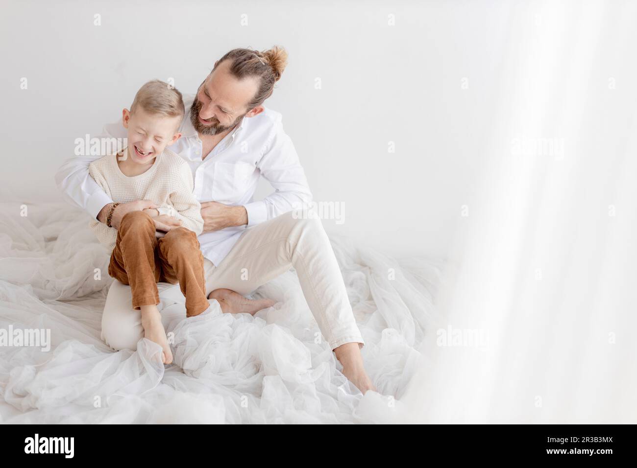Man tickling son sitting near white wall Stock Photo