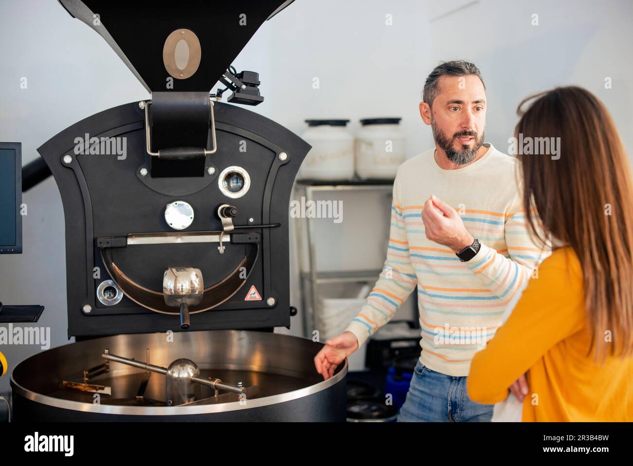 Man explaining woman standing near coffee grinder at cafe Stock Photo