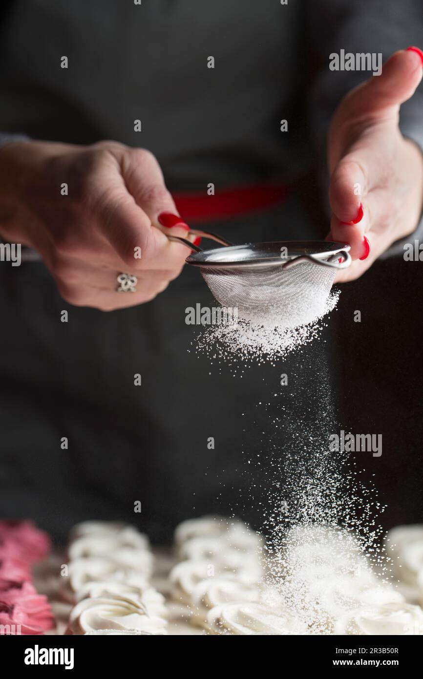 The process of making marshmallow. Close up hands of the chef with metal sieve sprinkling zephyr