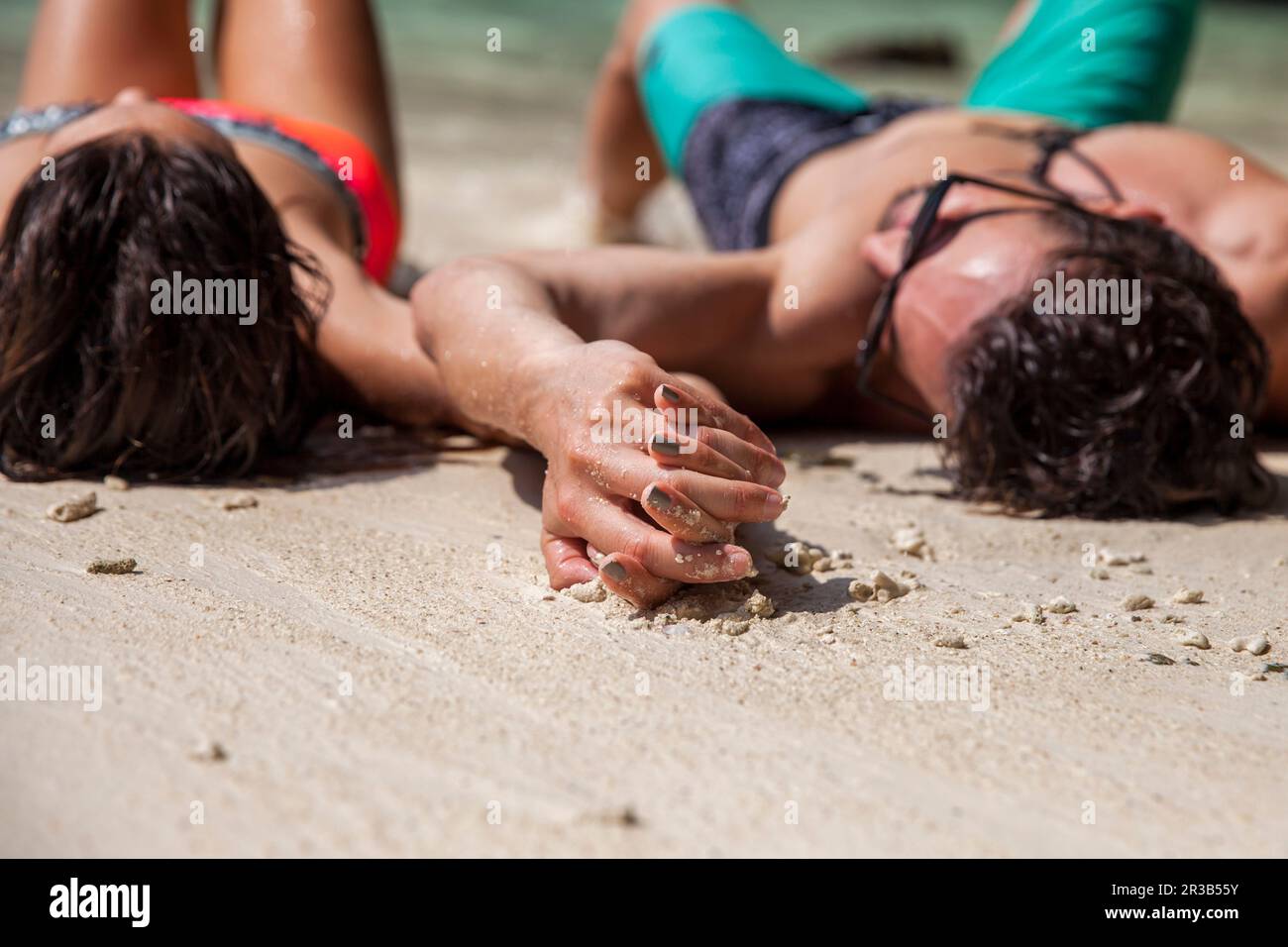 Couple holding hands lying on sand at beach Stock Photo