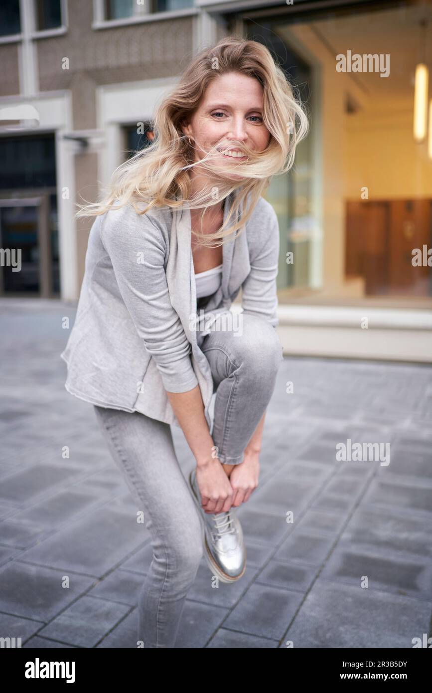 Smiling woman tying shoelace on footpath Stock Photo