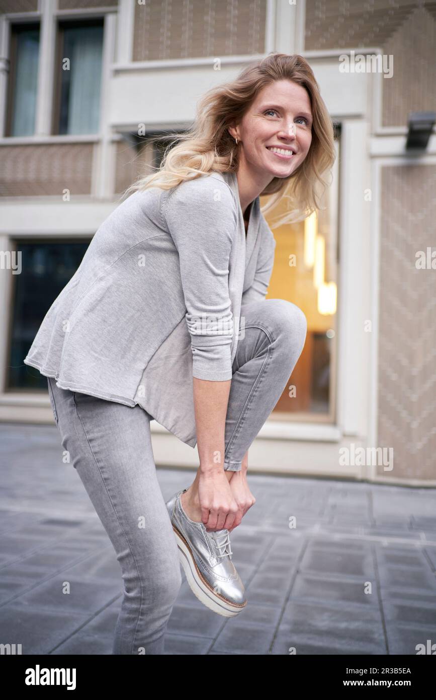 Blond woman tying shoelace standing on one leg Stock Photo