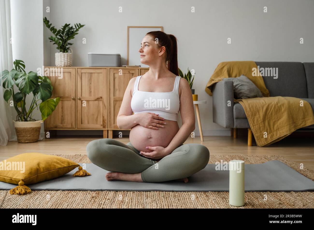 Pregnant woman sitting crosslegged with hands on stomach at home Stock Photo Alamy