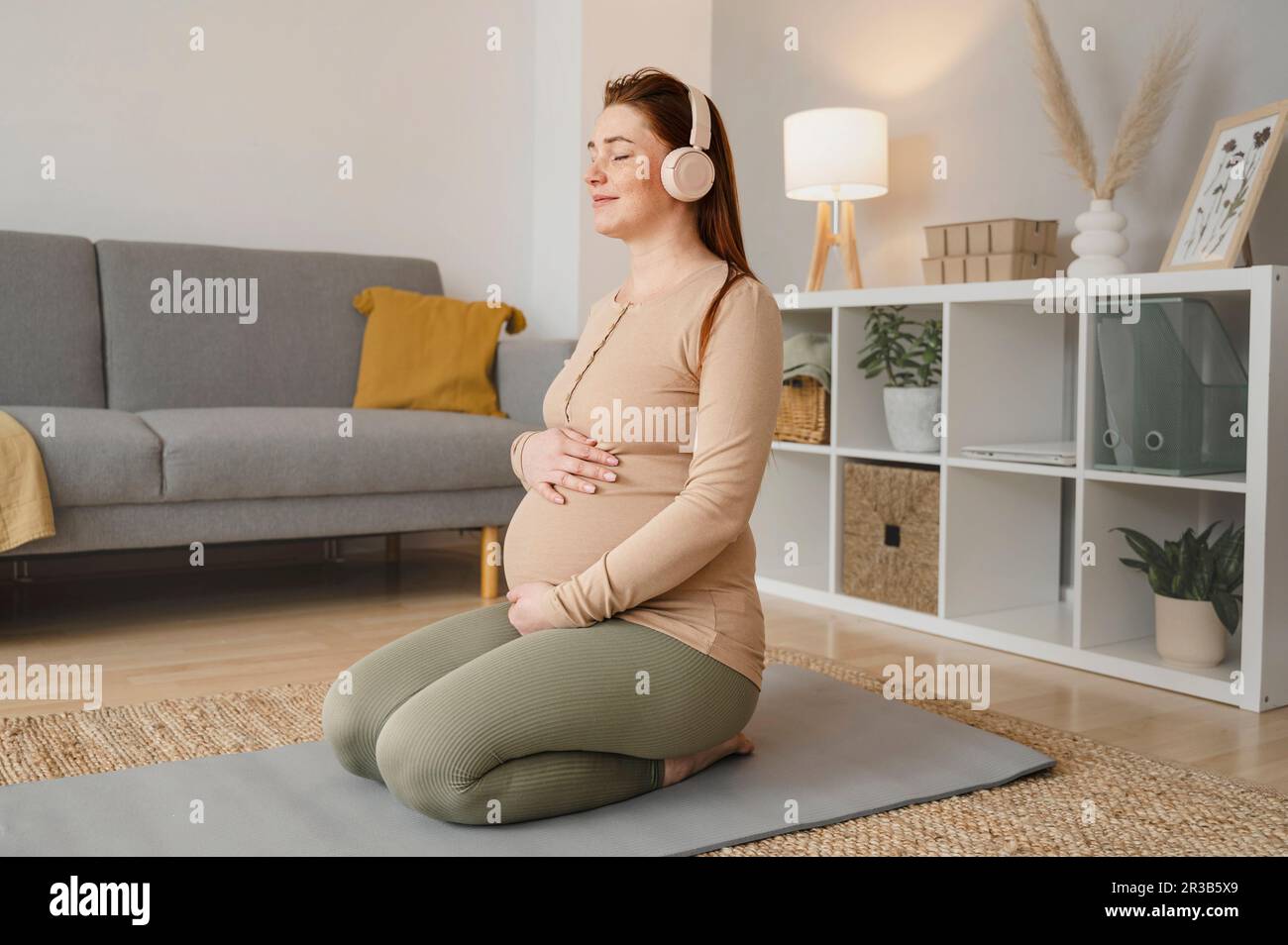 Pregnant woman listening to music sitting on exercise mat at home Stock ...