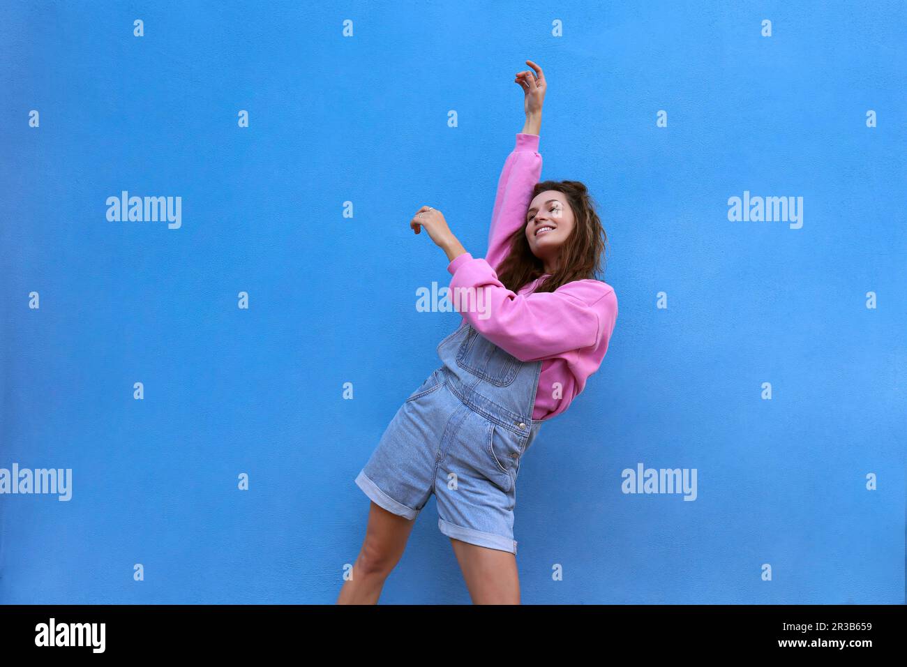 Carefree woman dancing against blue background Stock Photo