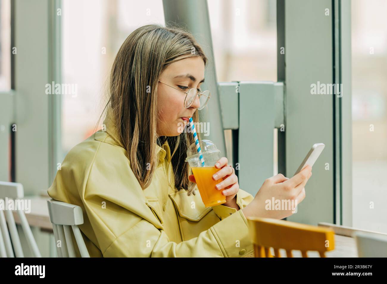 Teenage girl using phone and drinking juice in school cafeteria Stock