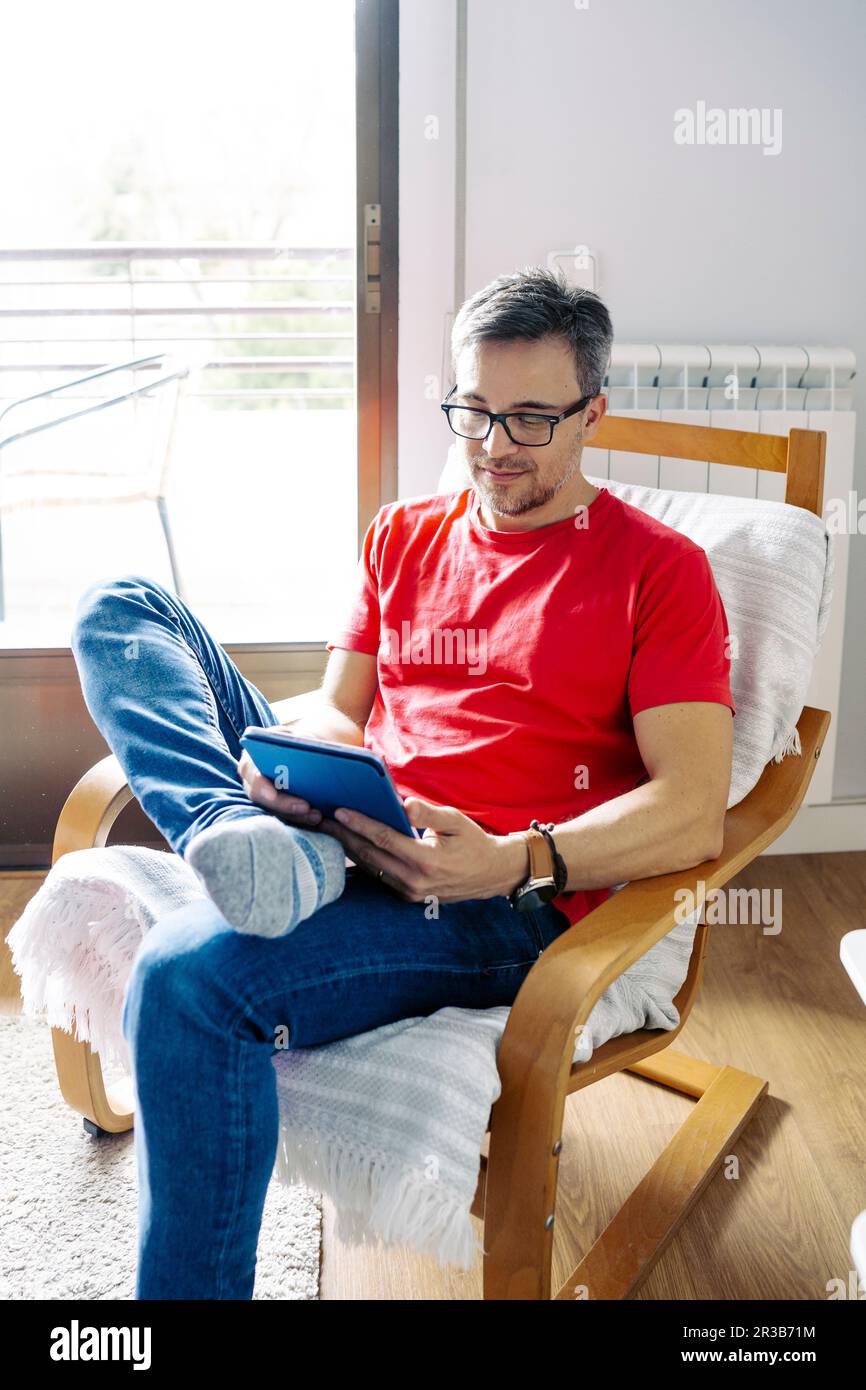 Man using tablet PC sitting on chair at home Stock Photo