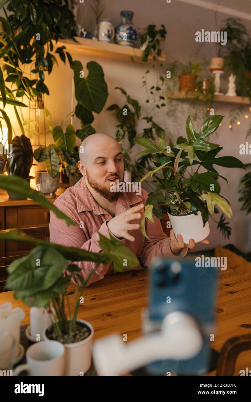 Man holding potted plant and vlogging through smart phone at home Stock ...