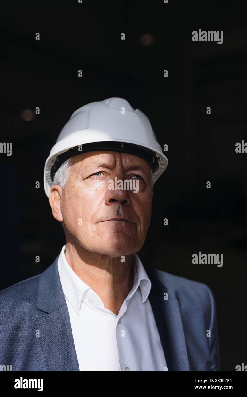 Thoughtful senior businessman wearing hard hat in factory Stock Photo