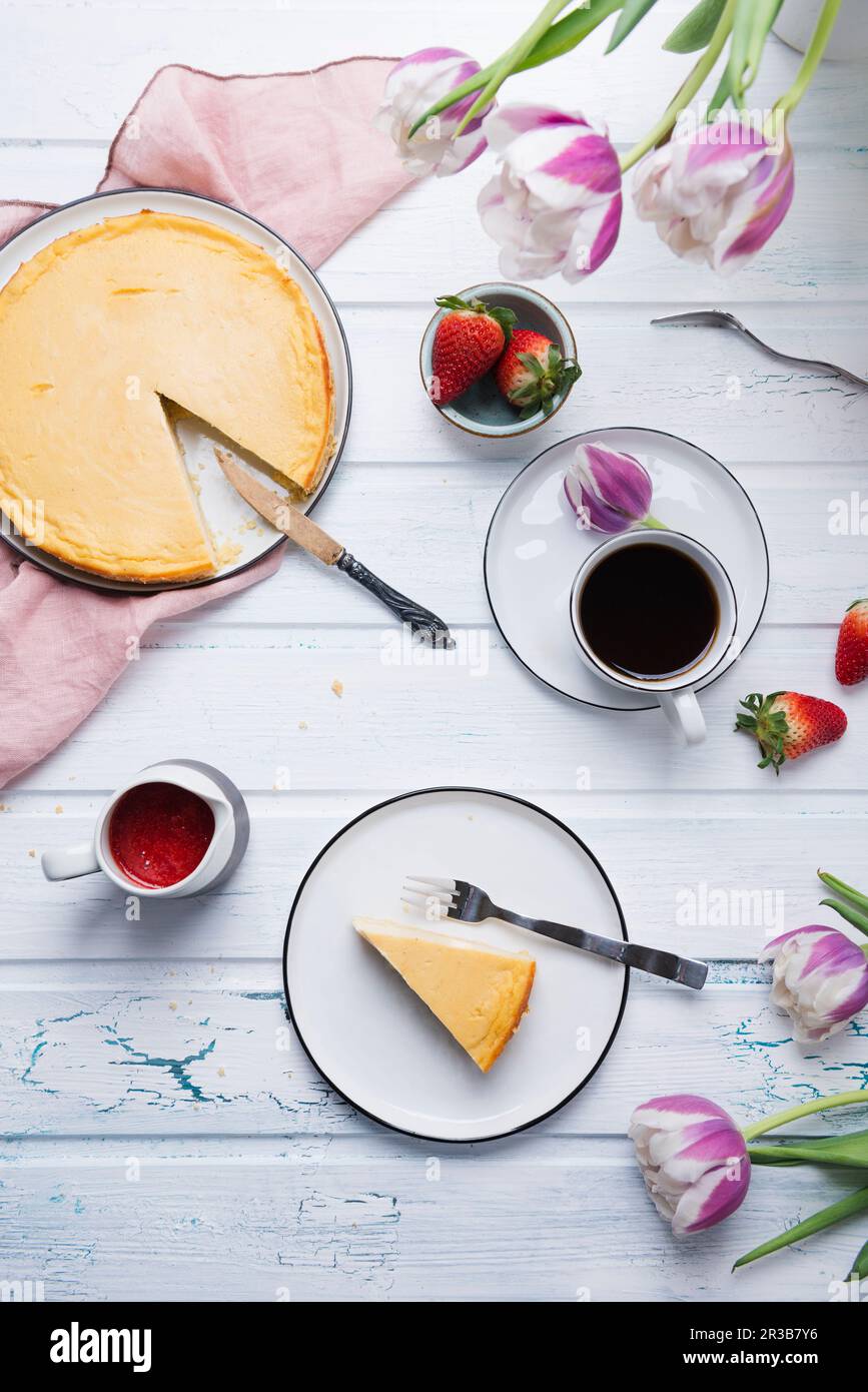Coffee served with vegan cheesecake, fresh fruits, strawberry sauce, and tulips Stock Photo