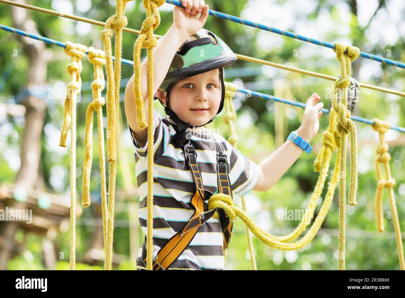 Kids climbing in adventure park. Boy enjoys climbing in the ropes course adventure. Child climbing h Stock Photo