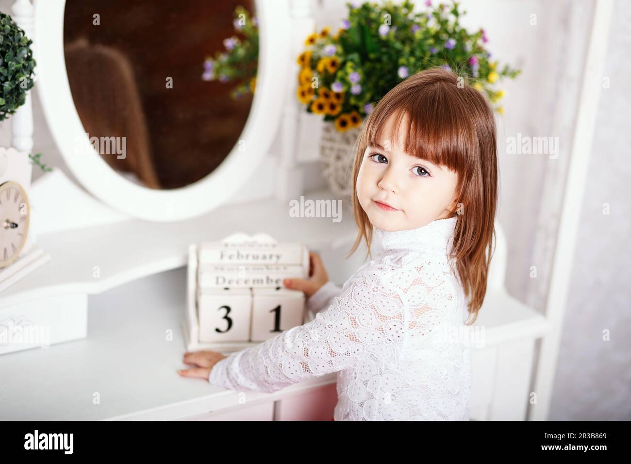 Portrait of a cute little girl sitting near a mirror with wooden calendar in the hands in the interi Stock Photo