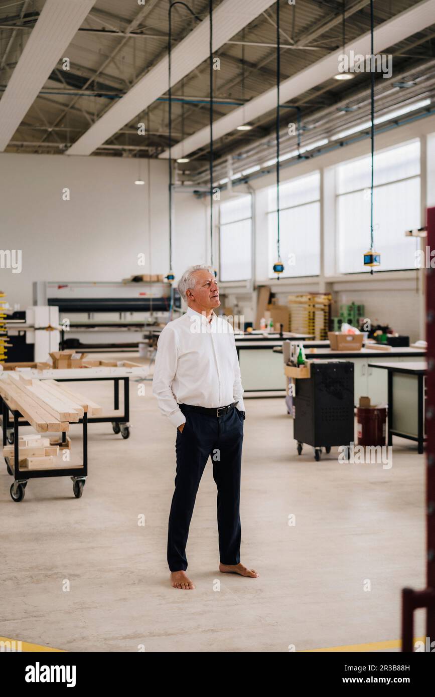 Senior businessman with hands in pockets standing on floor in industry Stock Photo