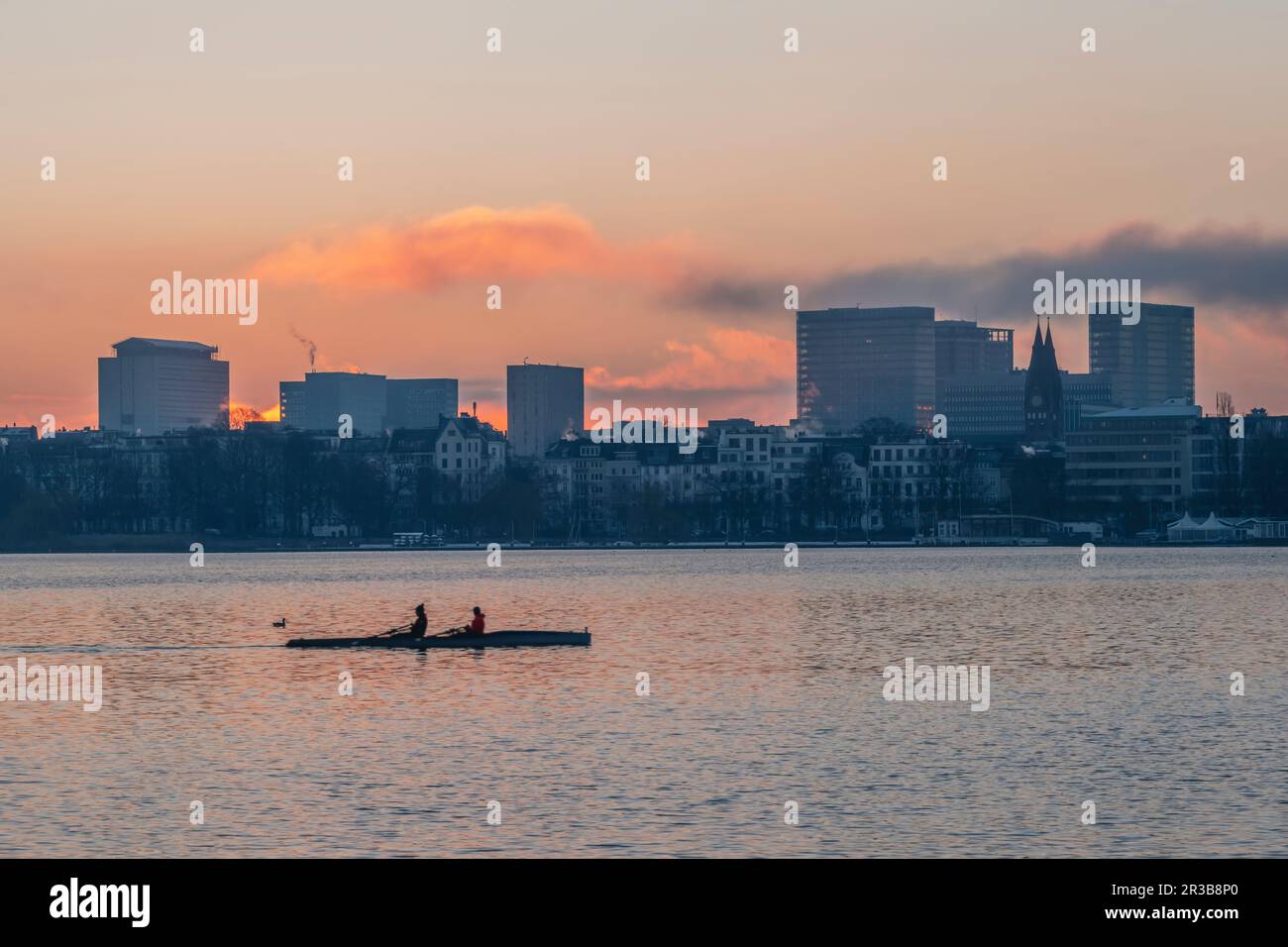Germany, Hamburg, Alster Lake at dawn with city skyline and rowing boat in background Stock Photo