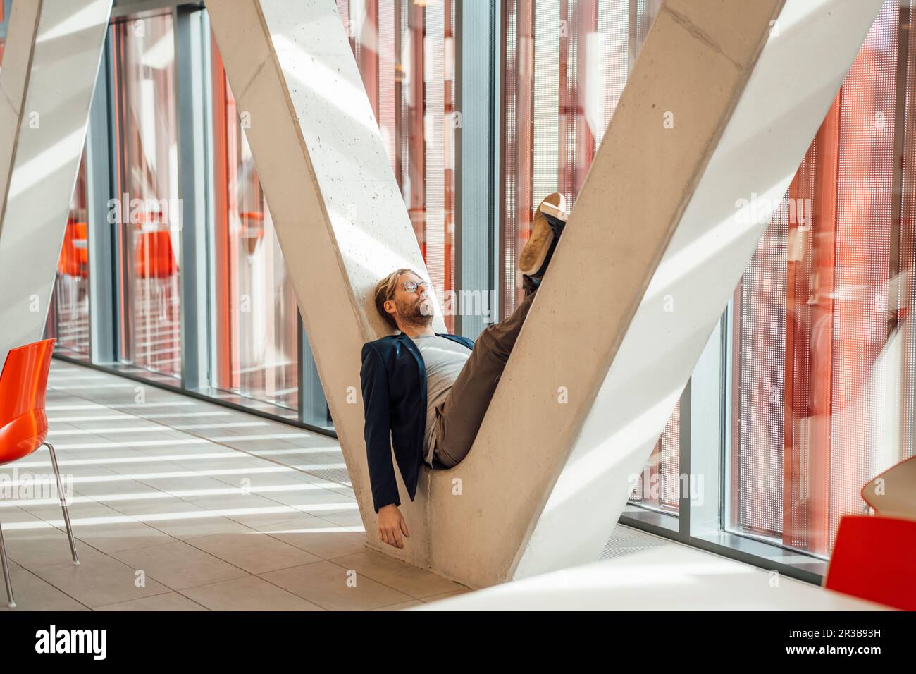 Businessman relaxing on V-shaped column in building Stock Photo