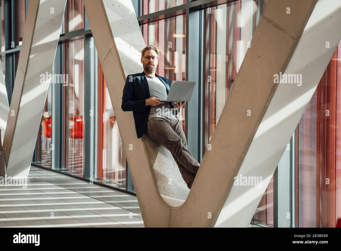 Businessman holding laptop leaning on V-shaped column in building Stock ...