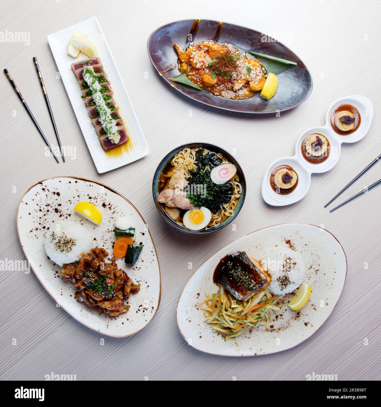 Japanese modern dishes on a table: Chicken Ramen, Tuna Tataki, Soba Chicken, Ebi Chilli Sauce, Grilled salmon and scallops with miso sauce Stock Photo