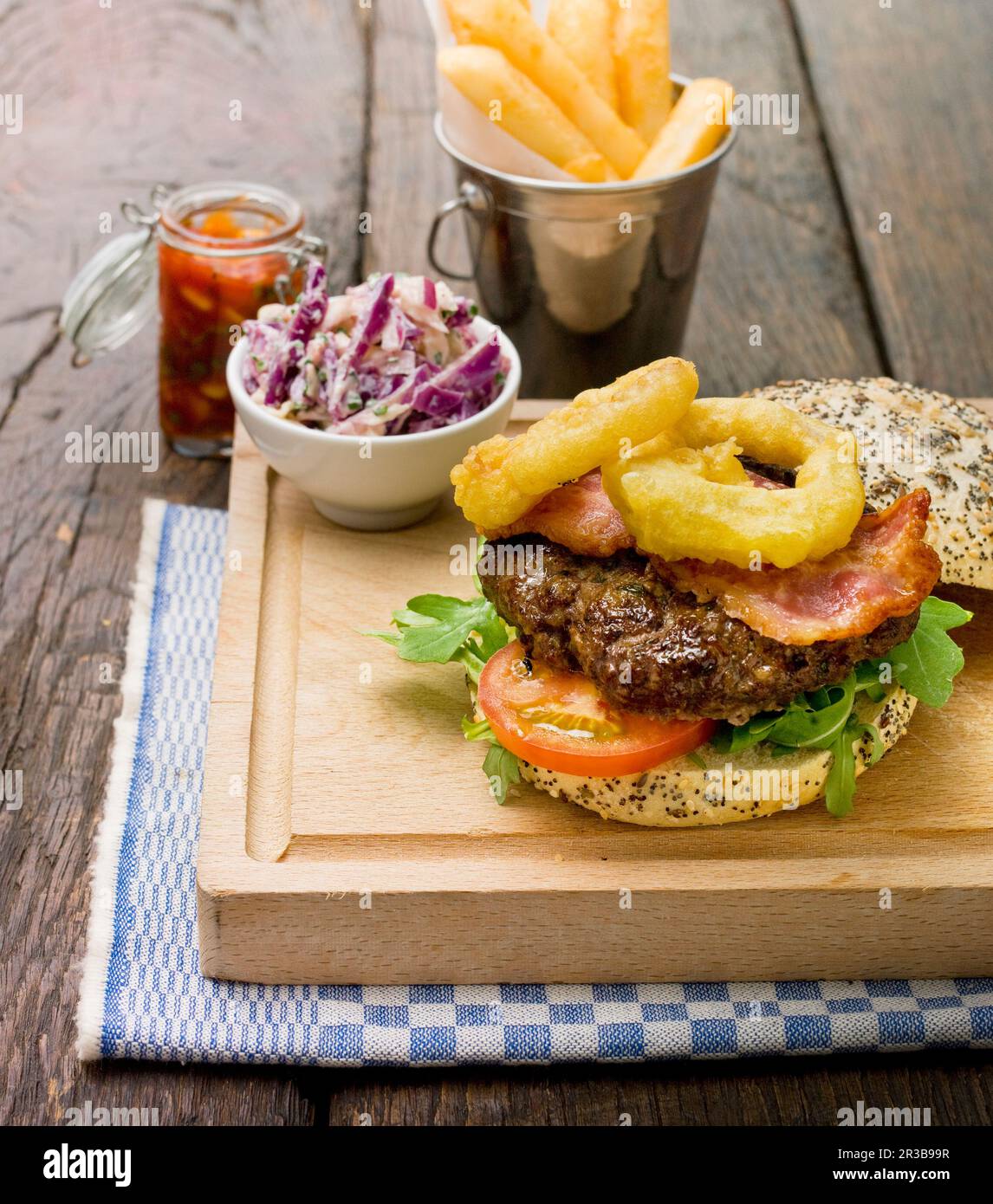 Home made burger with rocket lettuce, tomato, bacon and onion rings in ...