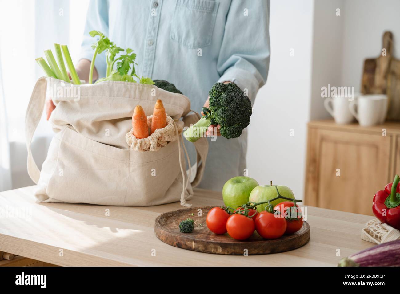 Woman holding broccoli by fresh fruits and vegetables on table at home ...