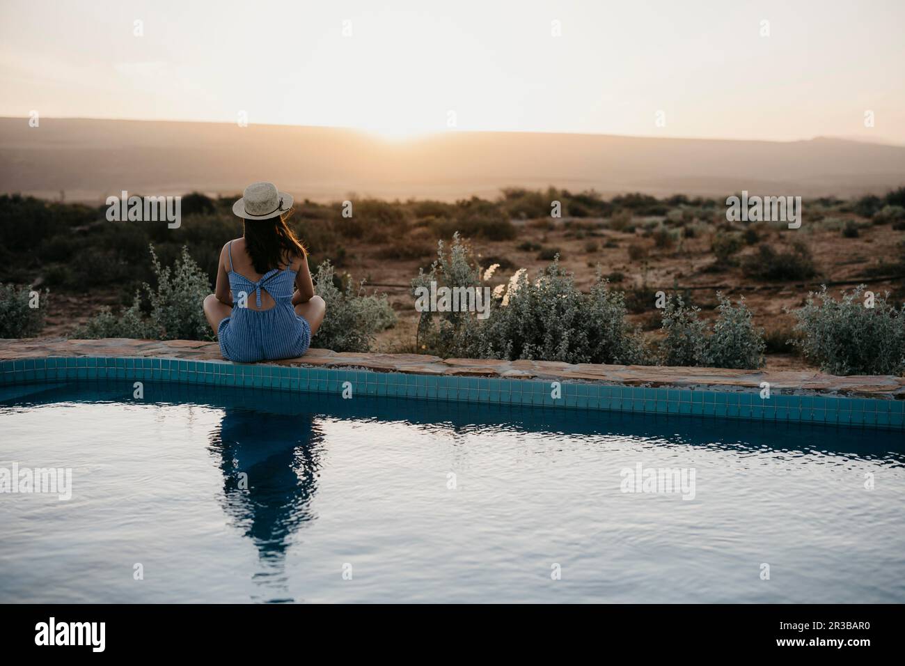 Woman looking at sunset sitting on poolside Stock Photo