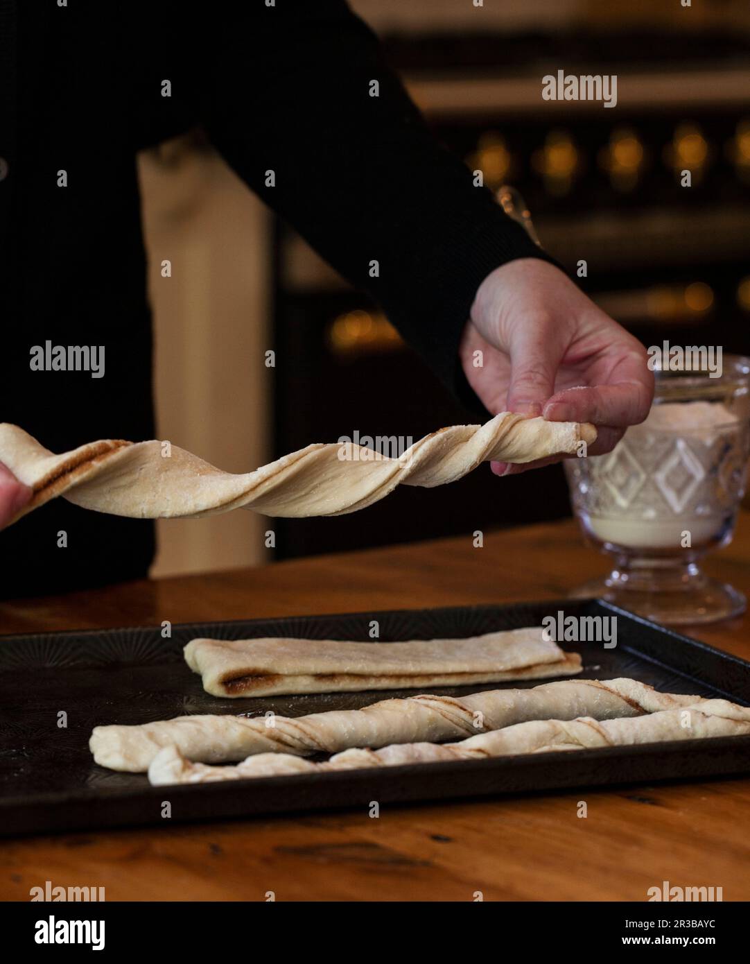 Woman twisting cinnamon bun dough into twists, on a baking sheet, with