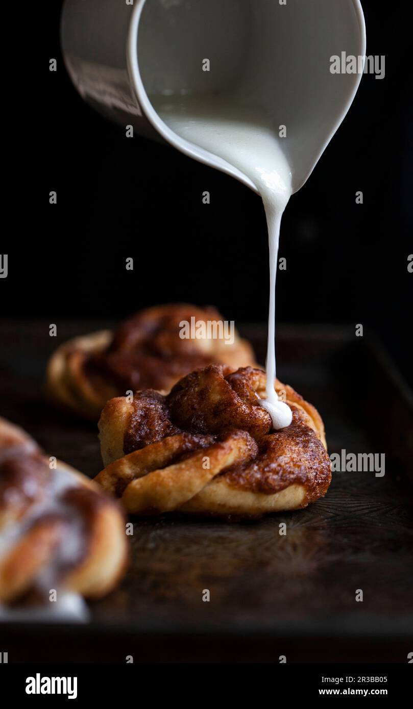 A cinnamon bun on a baking sheet being drizzled with icing Stock Photo