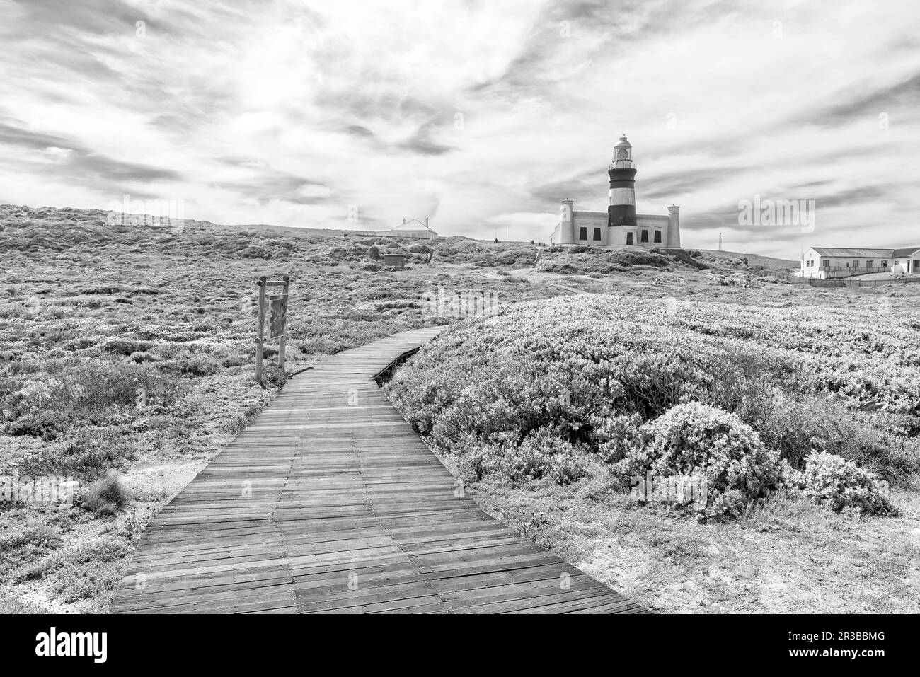The historic Agulhas lighthouse at the most southern tip of Africa, Cape Agulhas. The boardwalk to the lighthouse is visible. Monochrome Stock Photo