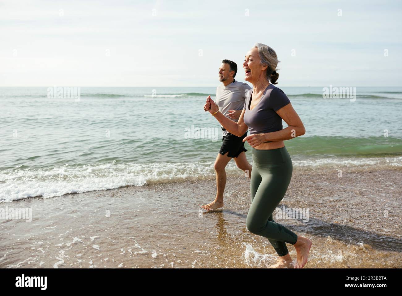 Happy mature couple laughing and running in water at beach Stock Photo