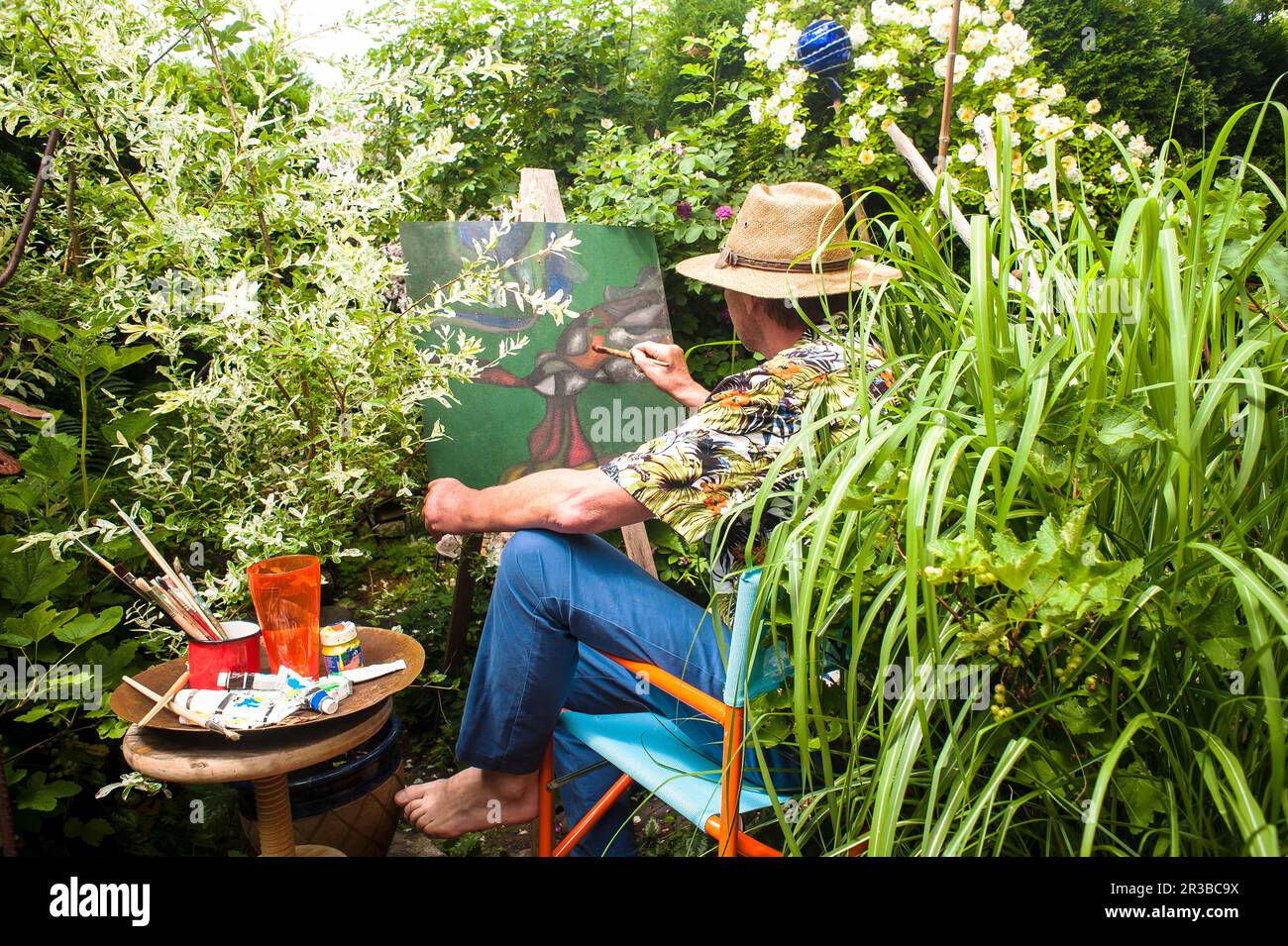 Man painting amidst plants sitting on chair in garden Stock Photo