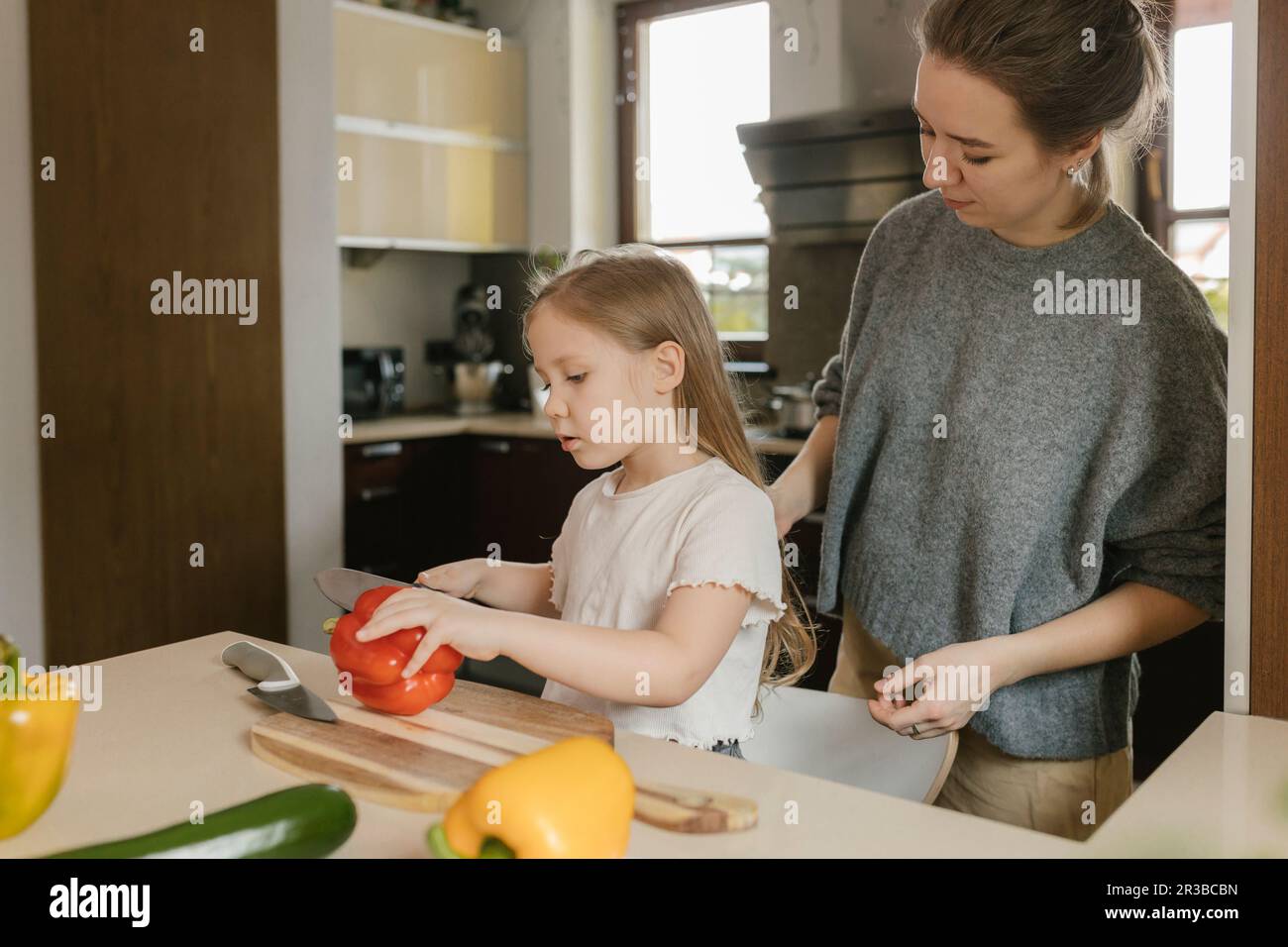 Mother with daughter cutting red bell pepper in kitchen at home Stock Photo