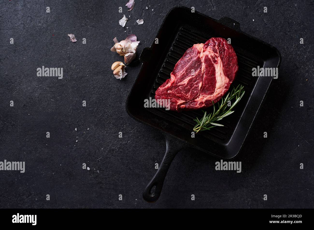 Black Angus prime beef chuck roll steak on cast iron grill skillet with fresh rosemary, thyme, olive oil, garlic and spices Stock Photo
