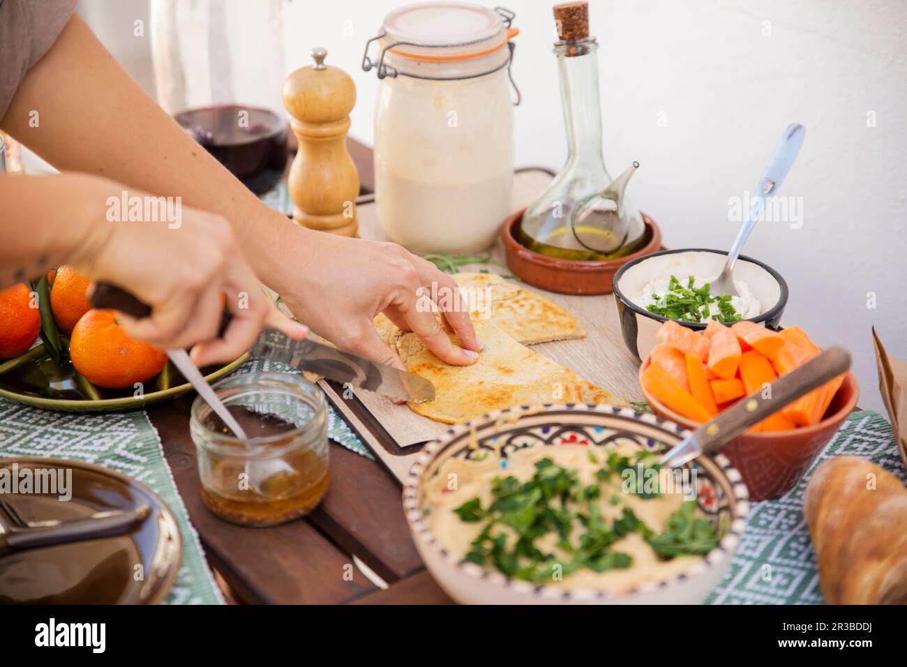 Hands cutting fermented bread surrounded with healthy meal in bowls and vegan products Stock Photo