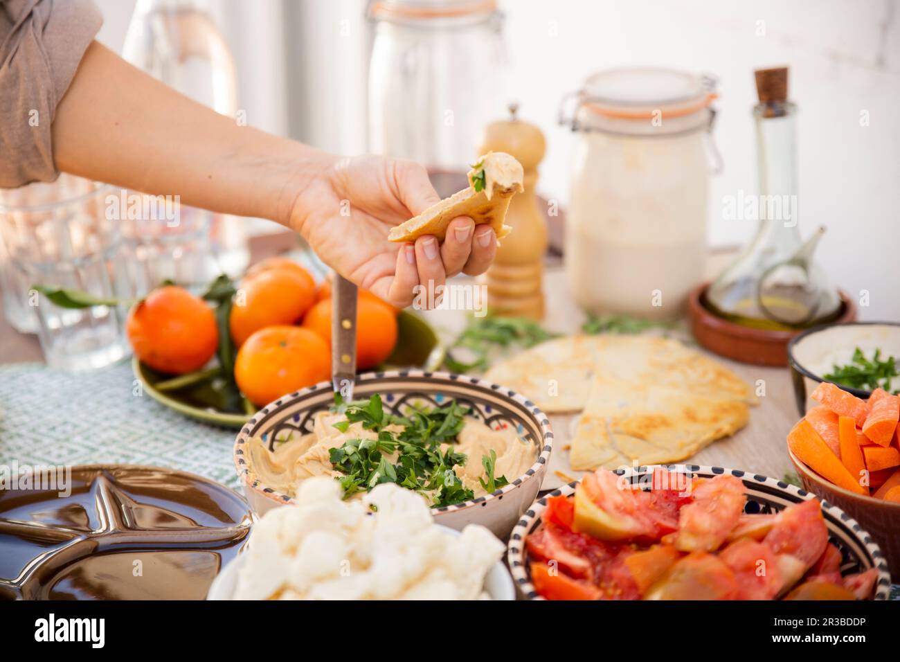 Hand holding hummus surrounded with healthy meal in bowls and vegan product Stock Photo