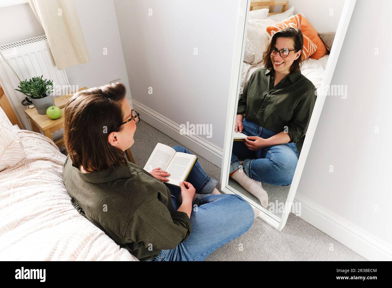 Happy woman sitting with book near mirror at home Stock Photo