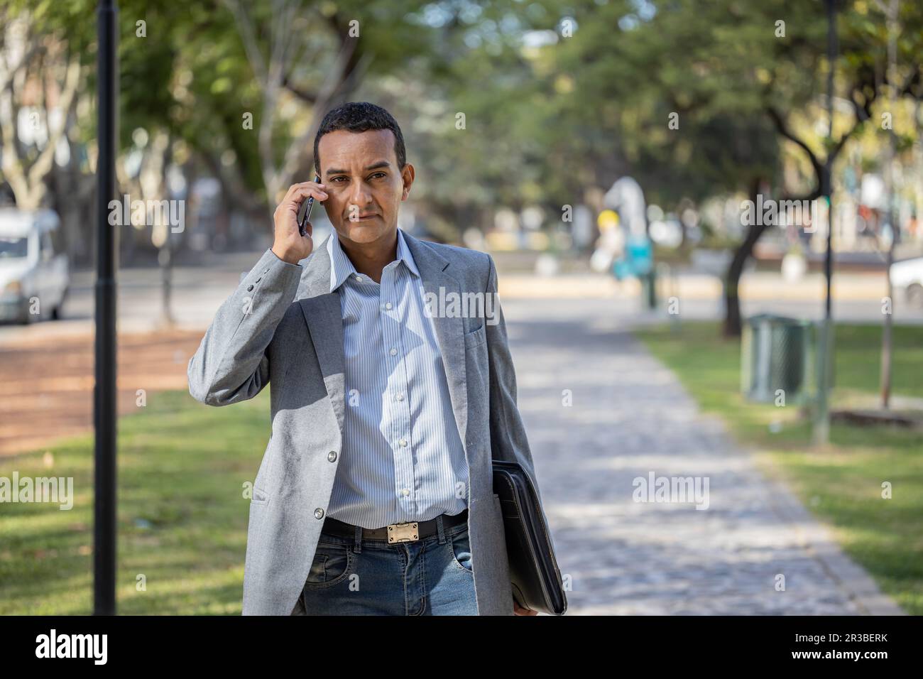 Young latin man in suit walking and talking on mobile phone with copy space. Stock Photo