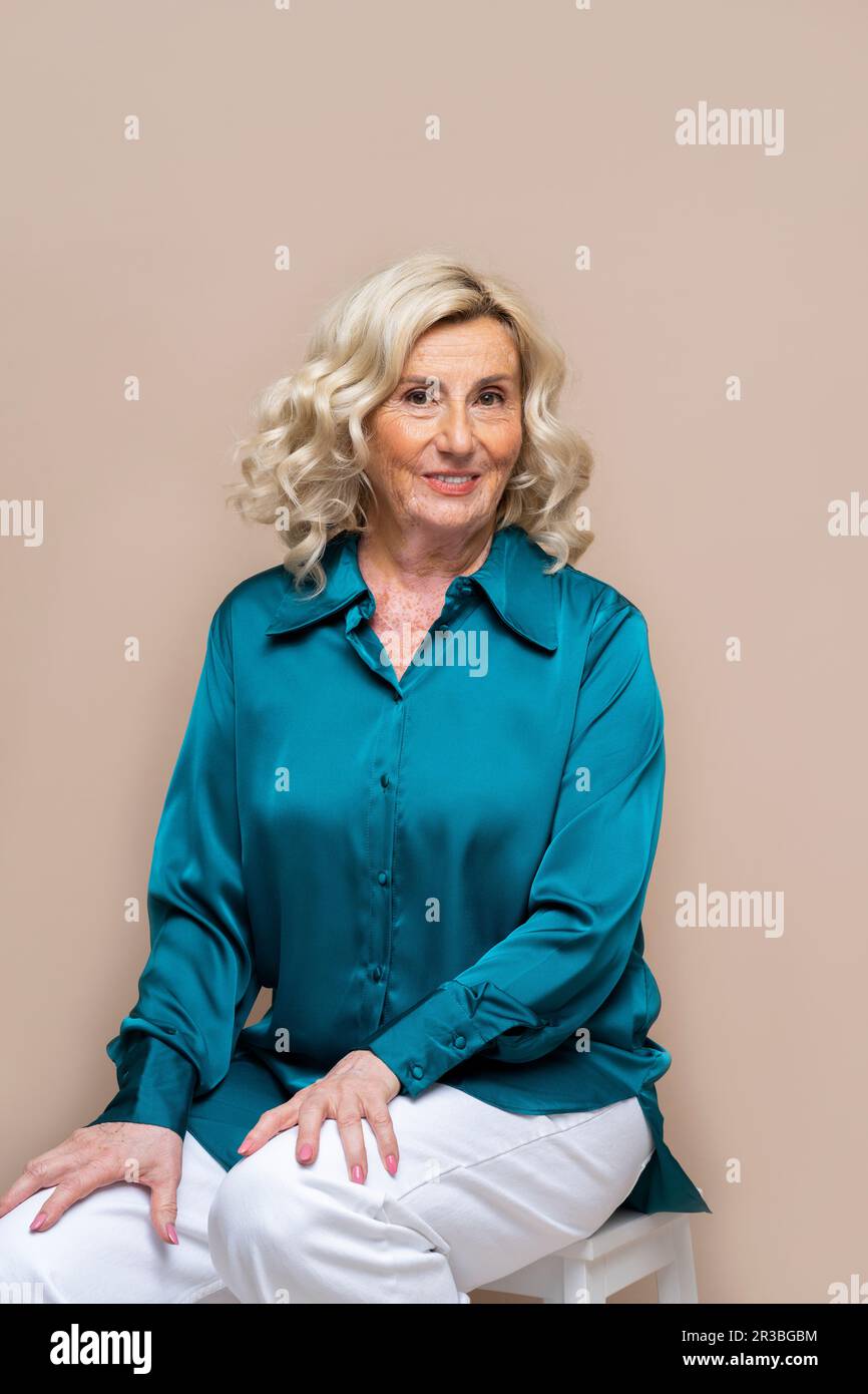 Senior woman sitting against beige background Stock Photo - Alamy