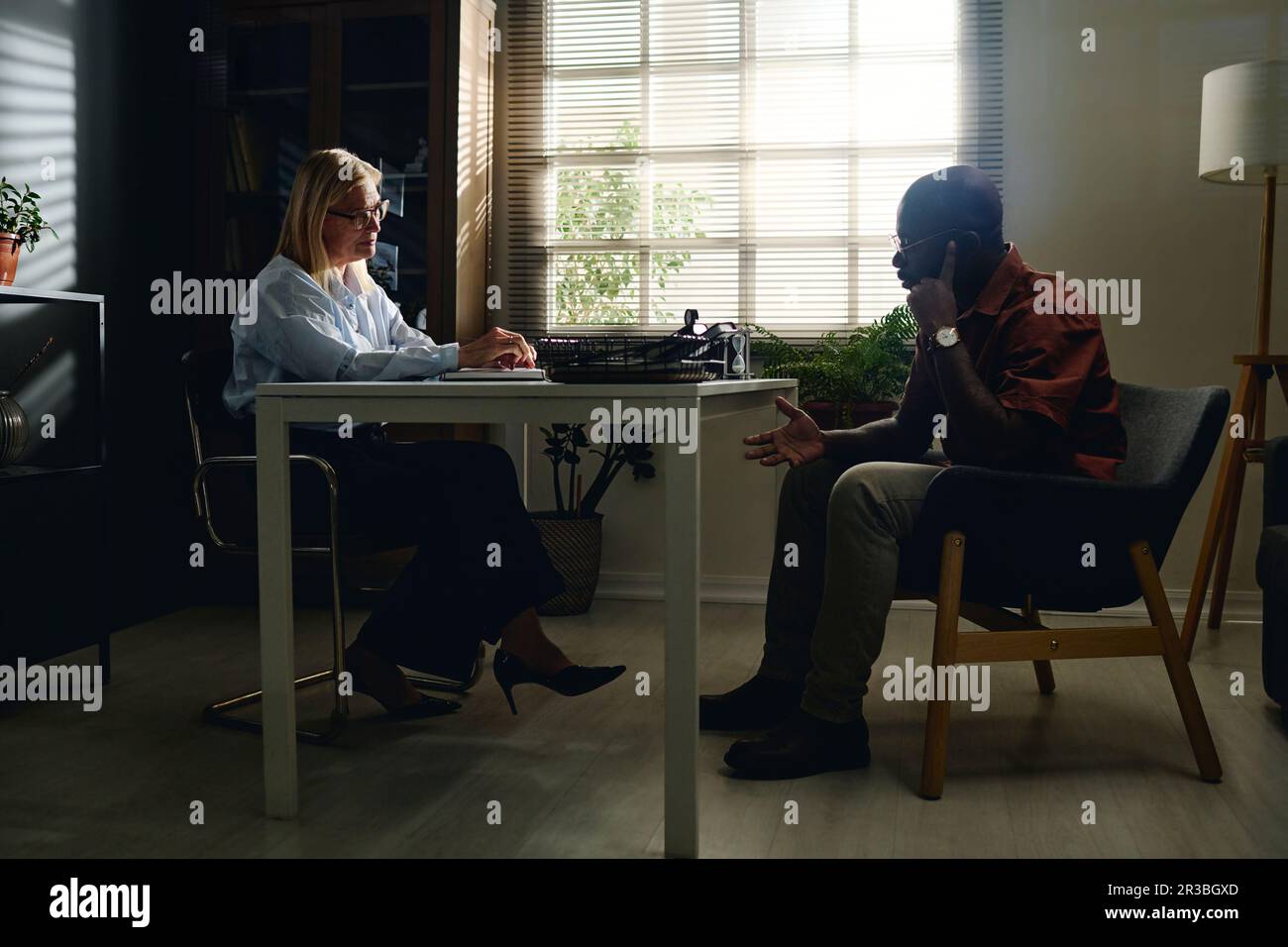 Patient discussing with psychologist sitting on chair at desk in office Stock Photo
