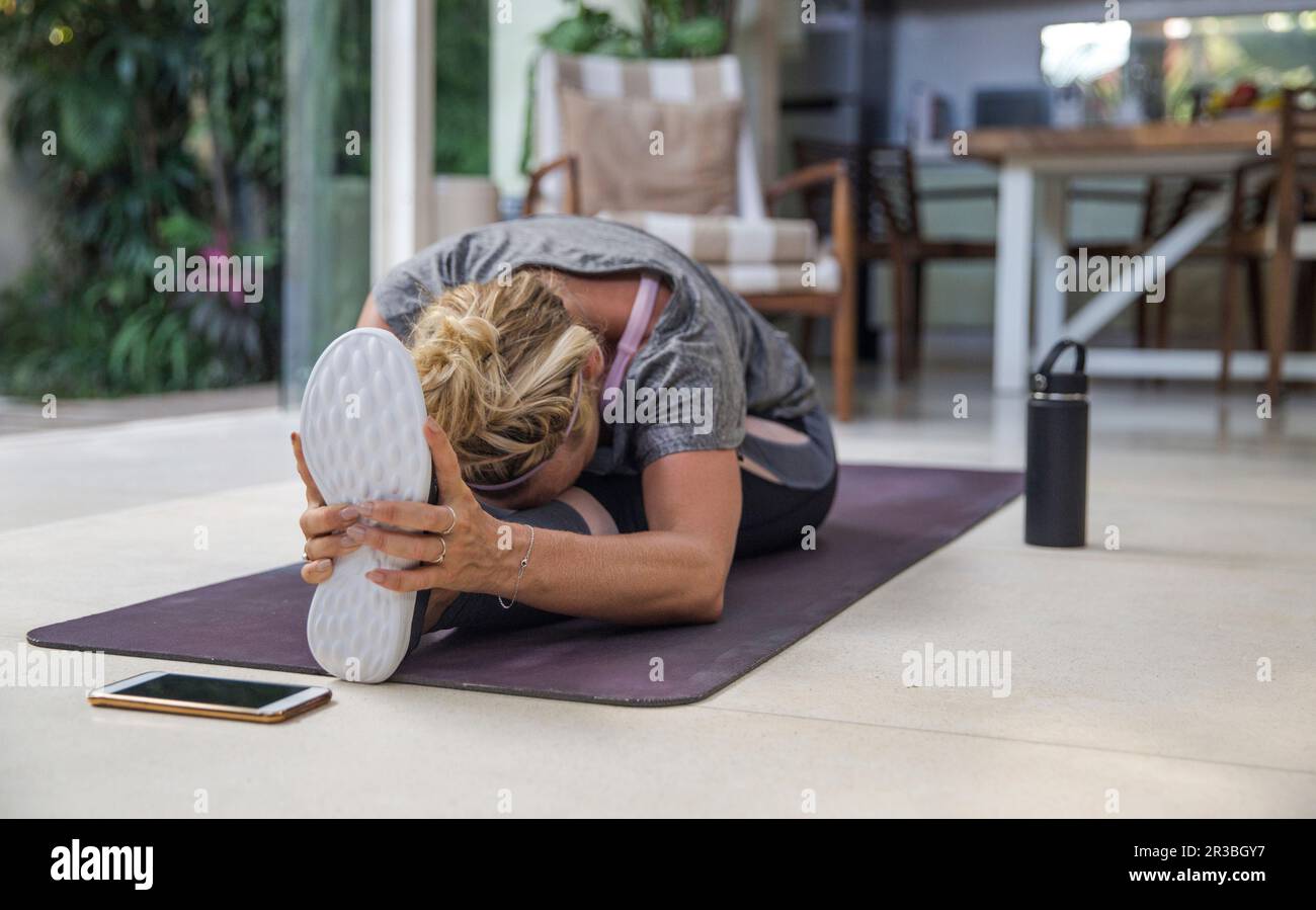 Woman practicing Janu Sirsasana on exercise mat at home Stock Photo