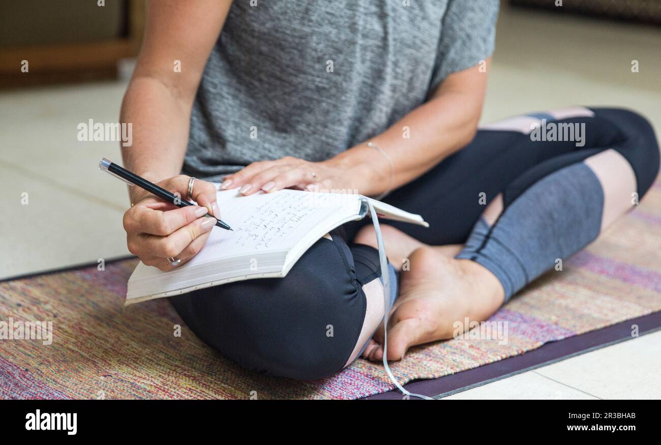 Woman writing in diary sitting cross-legged on exercise mat at home Stock Photo