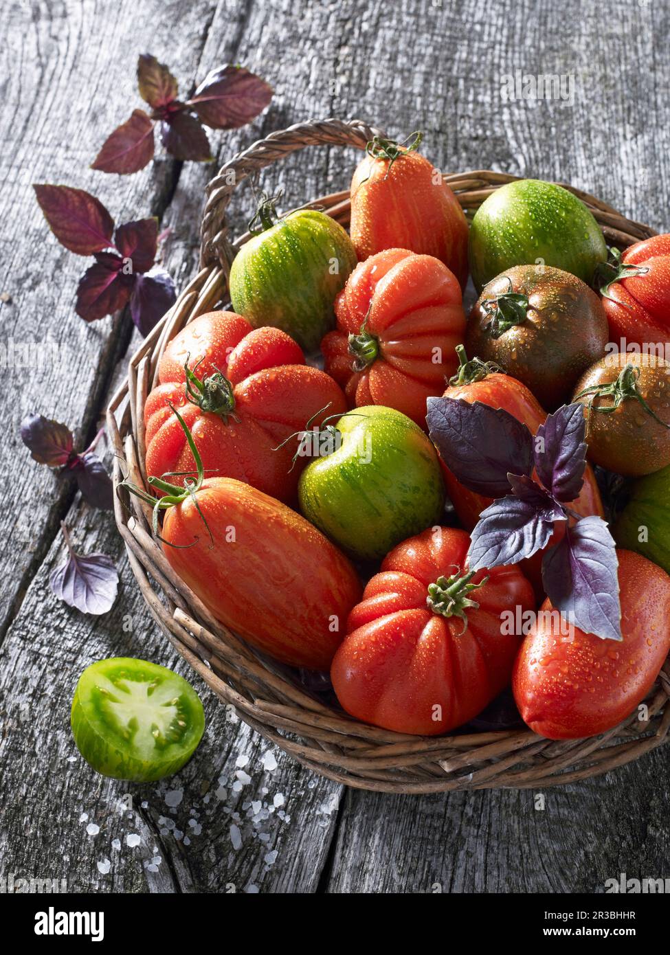 Various tomatoes with basil in a wicker basket Stock Photo - Alamy