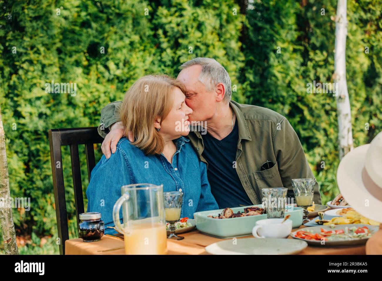 Senior man kissing woman sitting at dining table in back yard Stock Photo