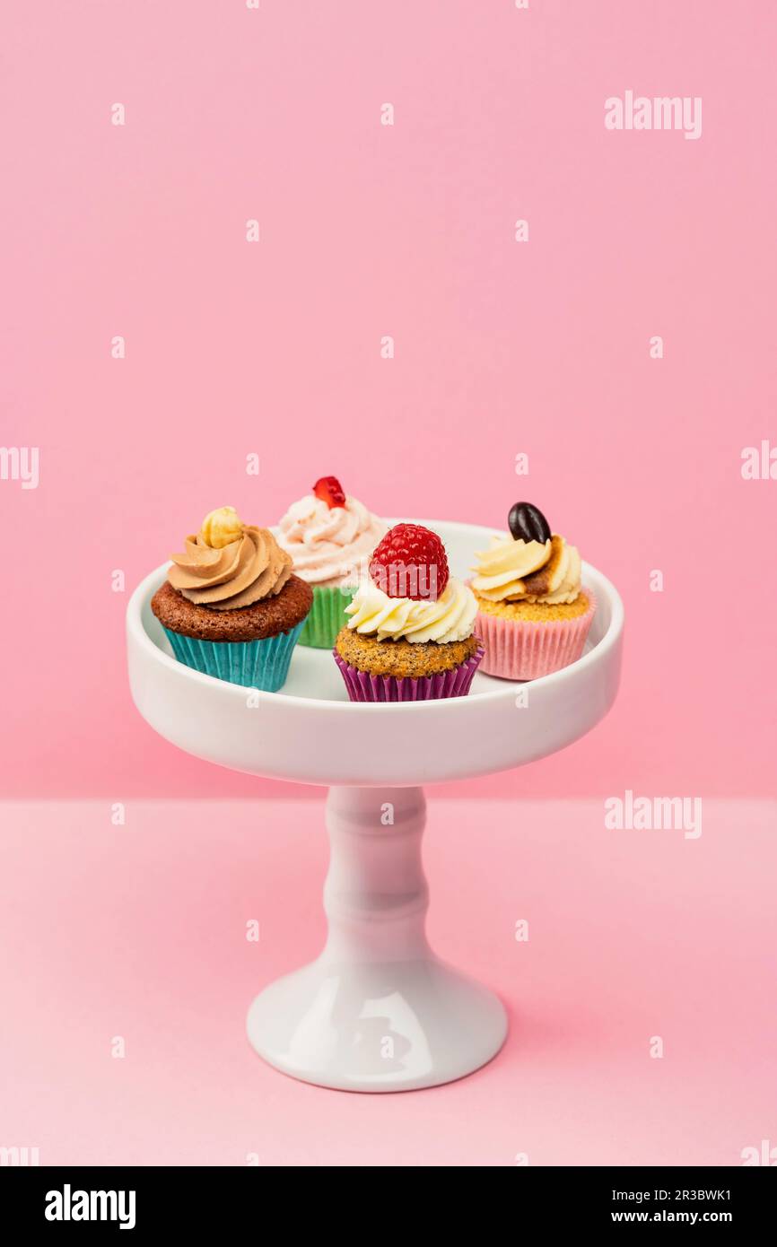 Assorted mini cupcakes on a cake stand against a pink background Stock Photo