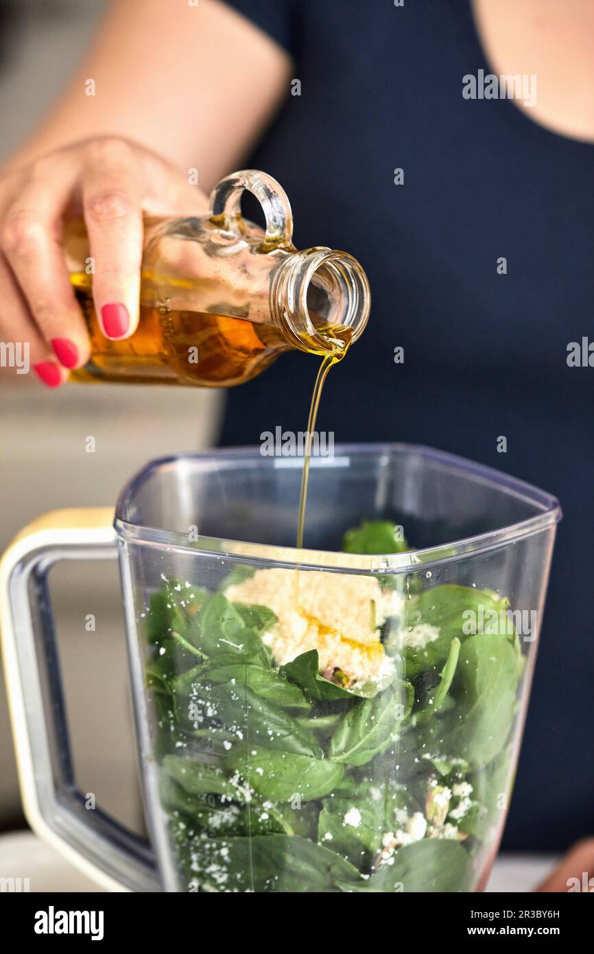 Pouring olive oil in food processor, making basil and arugula pesto Stock Photo