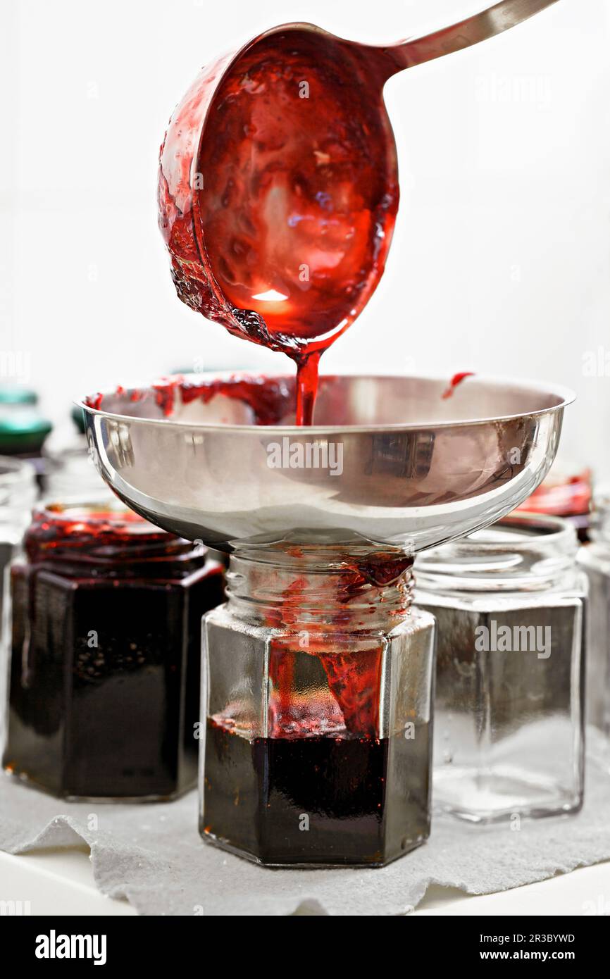 Pouring blackberry jam into glasses with a ladle and funnel Stock Photo