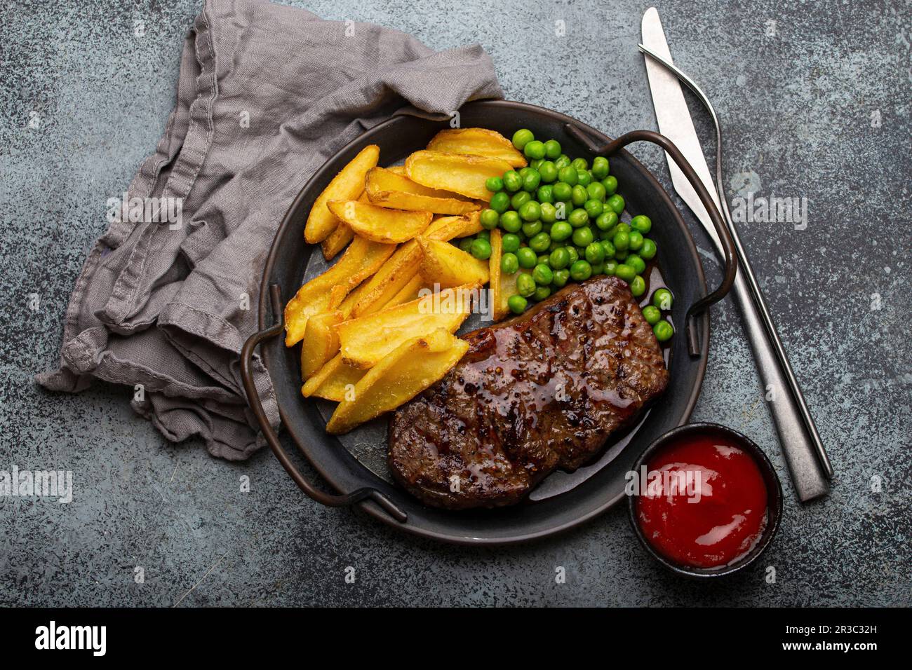 Grilled beef steak with potato chips french fries and green peas served with red tomato sauce Stock Photo